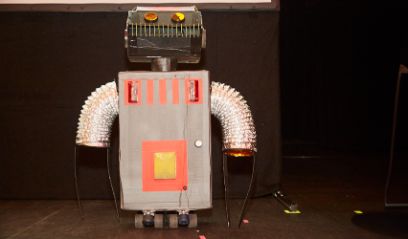 Ein selbstgebauter Roboter auf Rollen steht vor schwarzem Hintergrund.